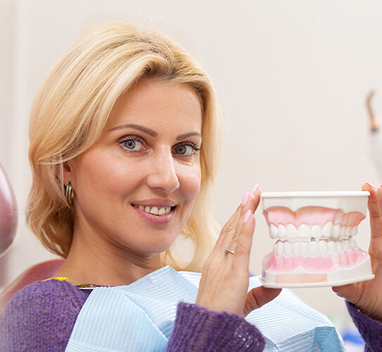 a lady holding a model of a jaw that portraits effect of regular teeth cleanings.