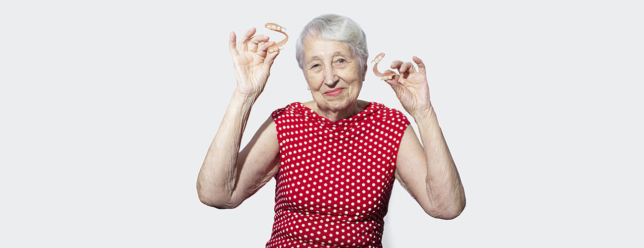 old lady holding dentures and smiling
