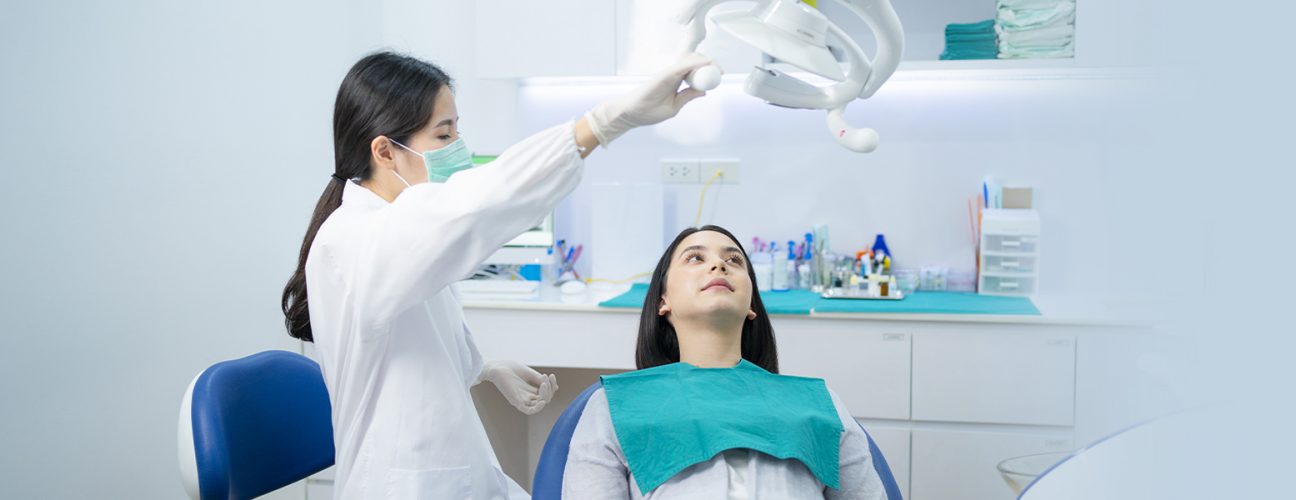 dentist is setting up to examine girl and girl is laying on dental chair